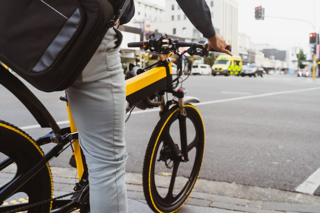 Rider on a yellow e-bike waiting at a city intersection, with an ambulance in traffic ahead
